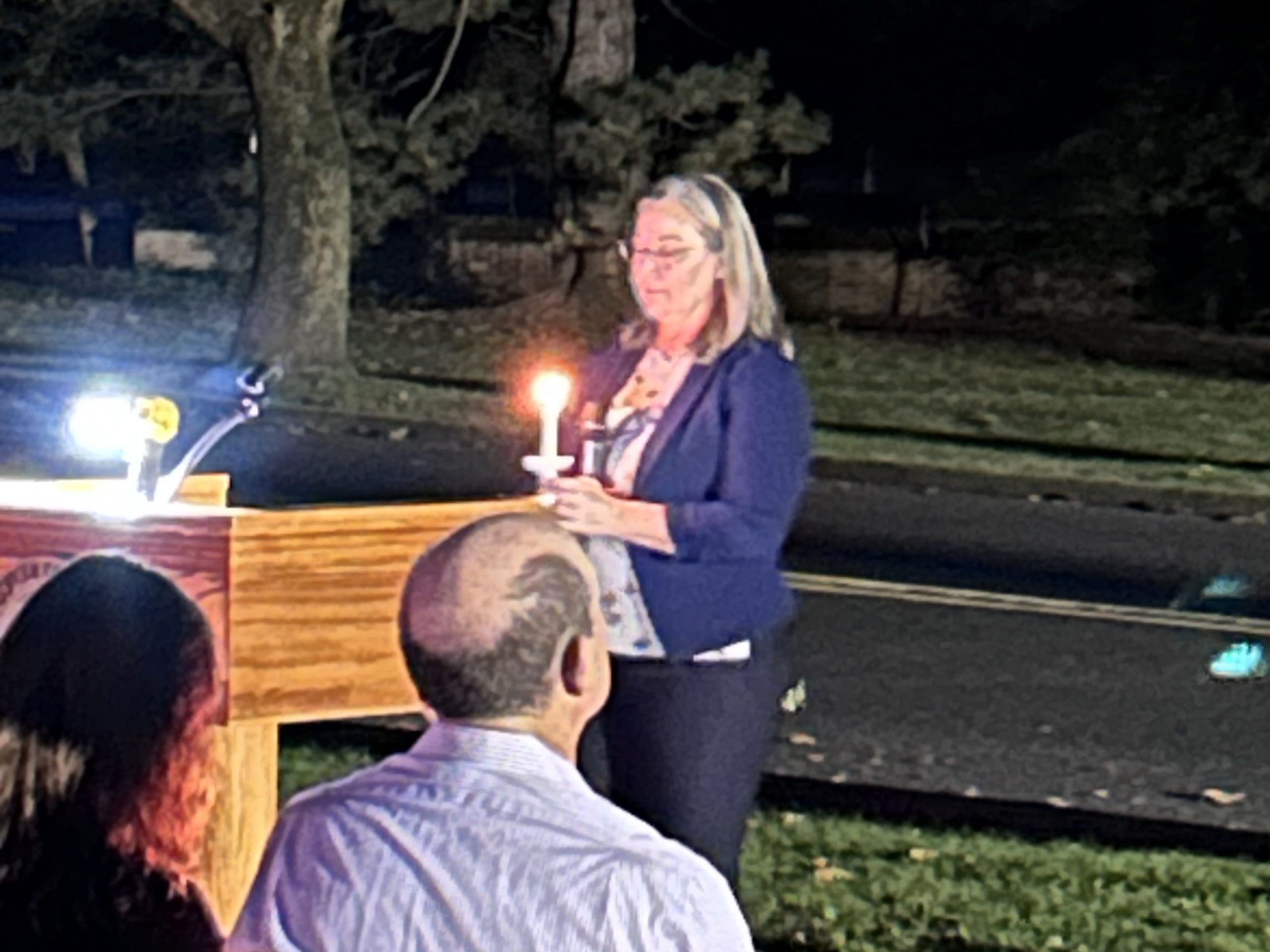 Executive Director Julye Myner standing at podium holding candle during 2023 Vigil